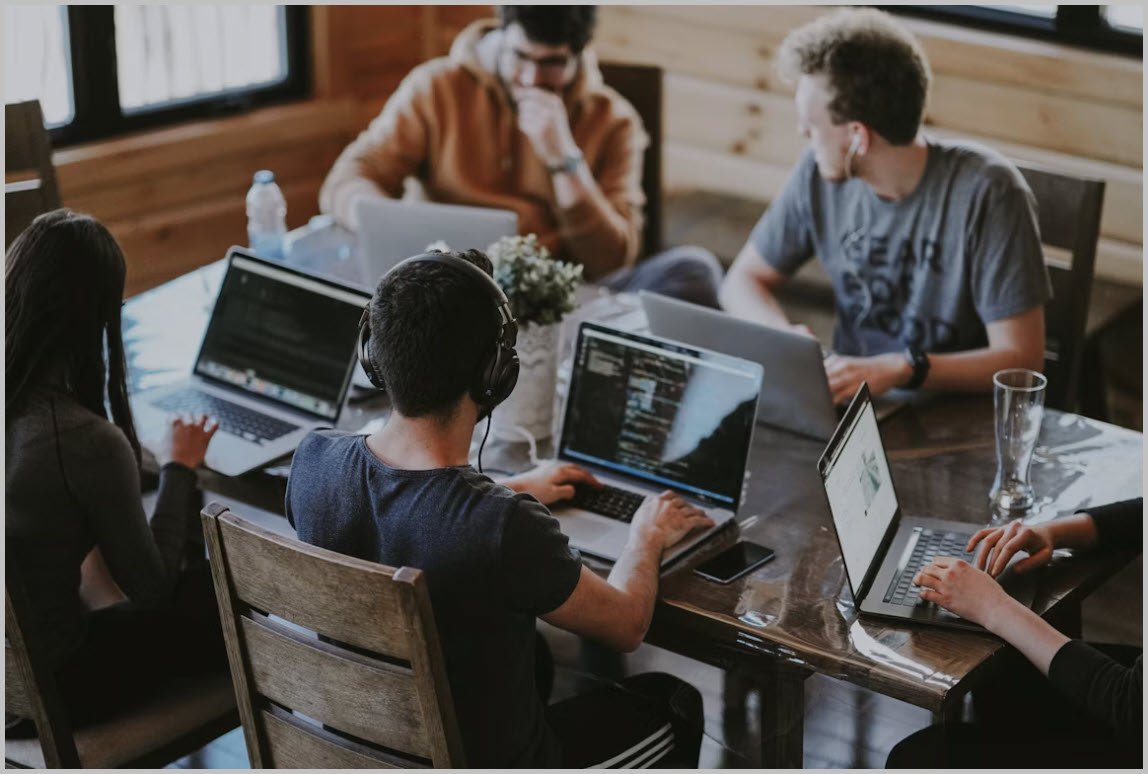 A team of engineers working together around a table of laptops